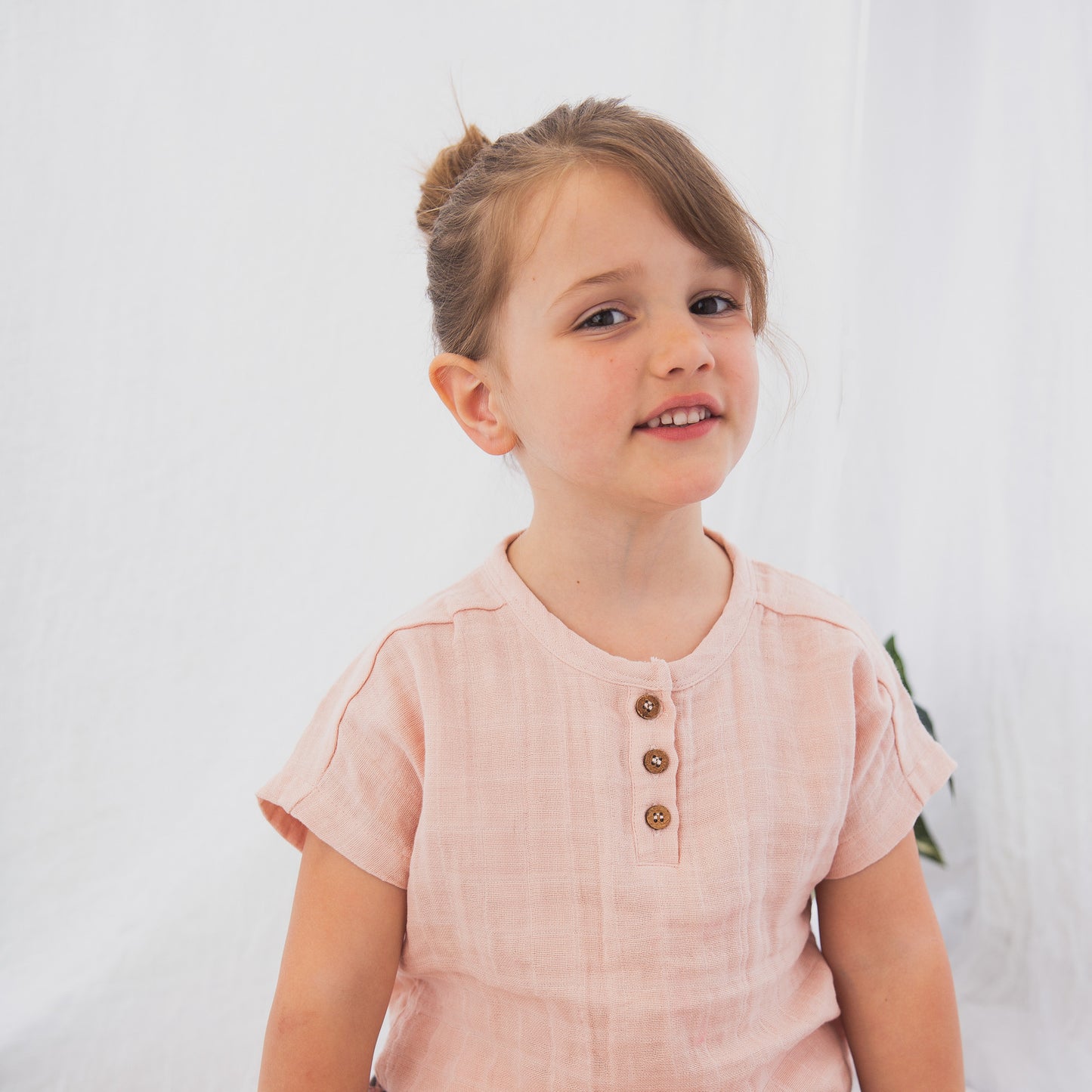 Girl standing against a white background, posing in wearing Jasper Muslin Top in Dusty Rose, designed by Burrow and Be.