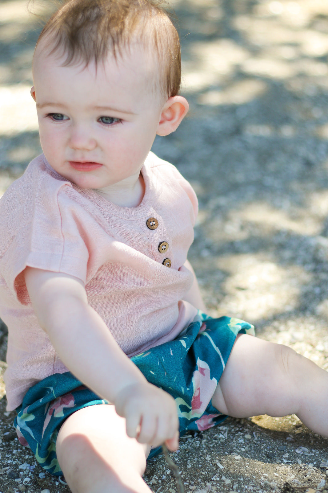 Girl sitting on the riverside, posing in Jasper Muslin Top in Dusty Rose and Green Leavings Lyla Shorts, both designed by Burrow and Be.