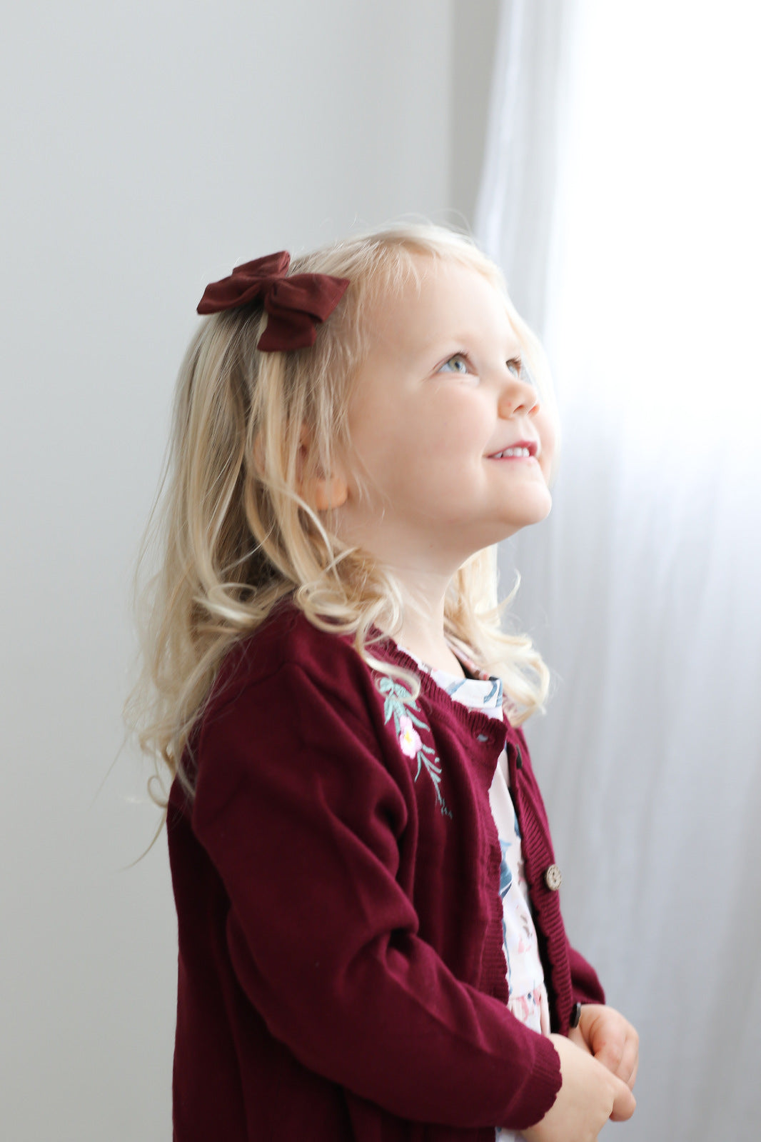 Girl standing in front of a white curtain and wearing Lola Knit Cardigan - Bloom, designed by Burrow and Be