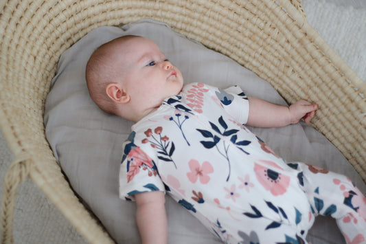 Newborn resting in a Moses basket in an organic cotton zip suit through the quiet confinement month, Burrow and Be Singapore
