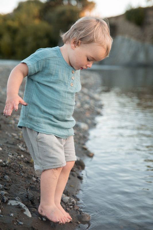 Child by the river in a breathable organic cotton top on a first family trip, Burrow and Be Singapore