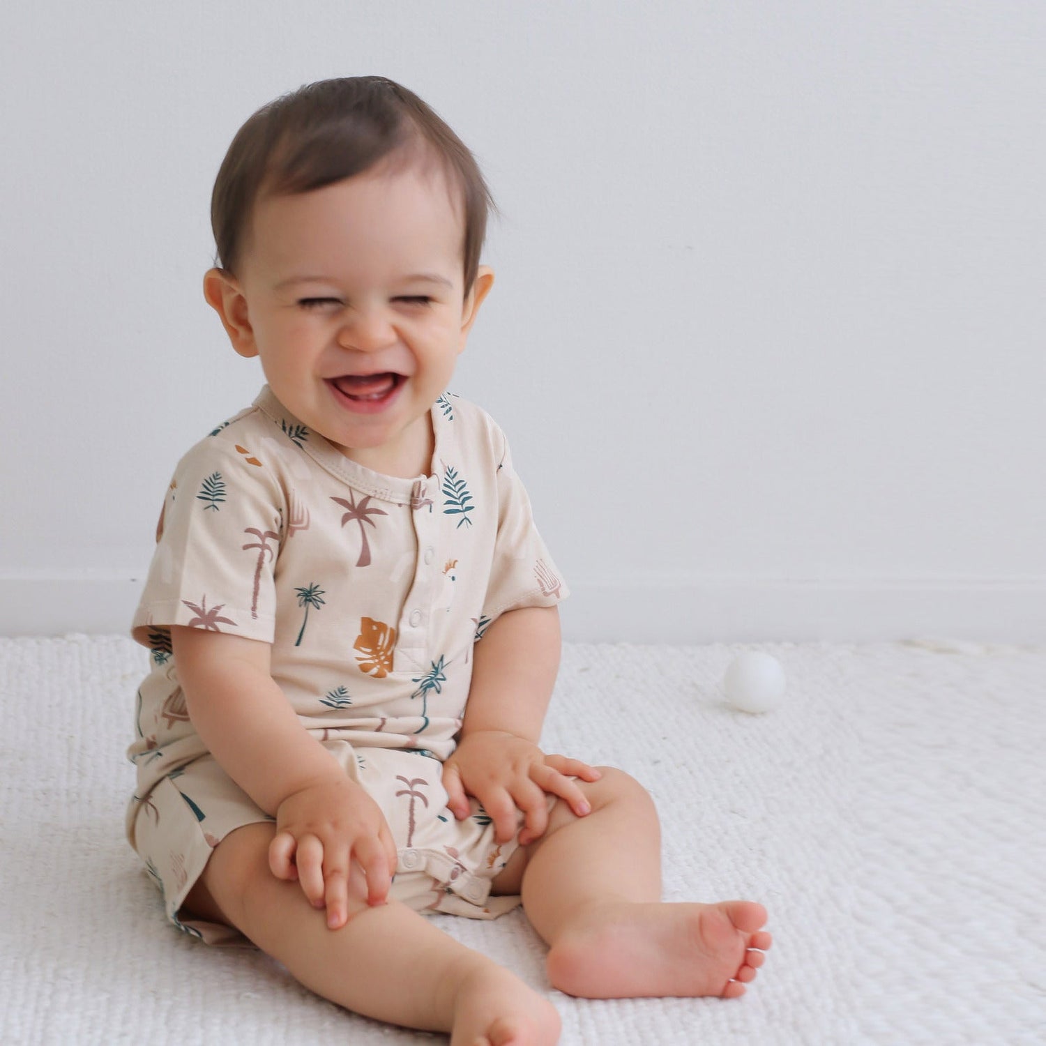 Baby sitting on floor and laughing while wearing Jungle Stamp Alex Romper from Burrow and Be