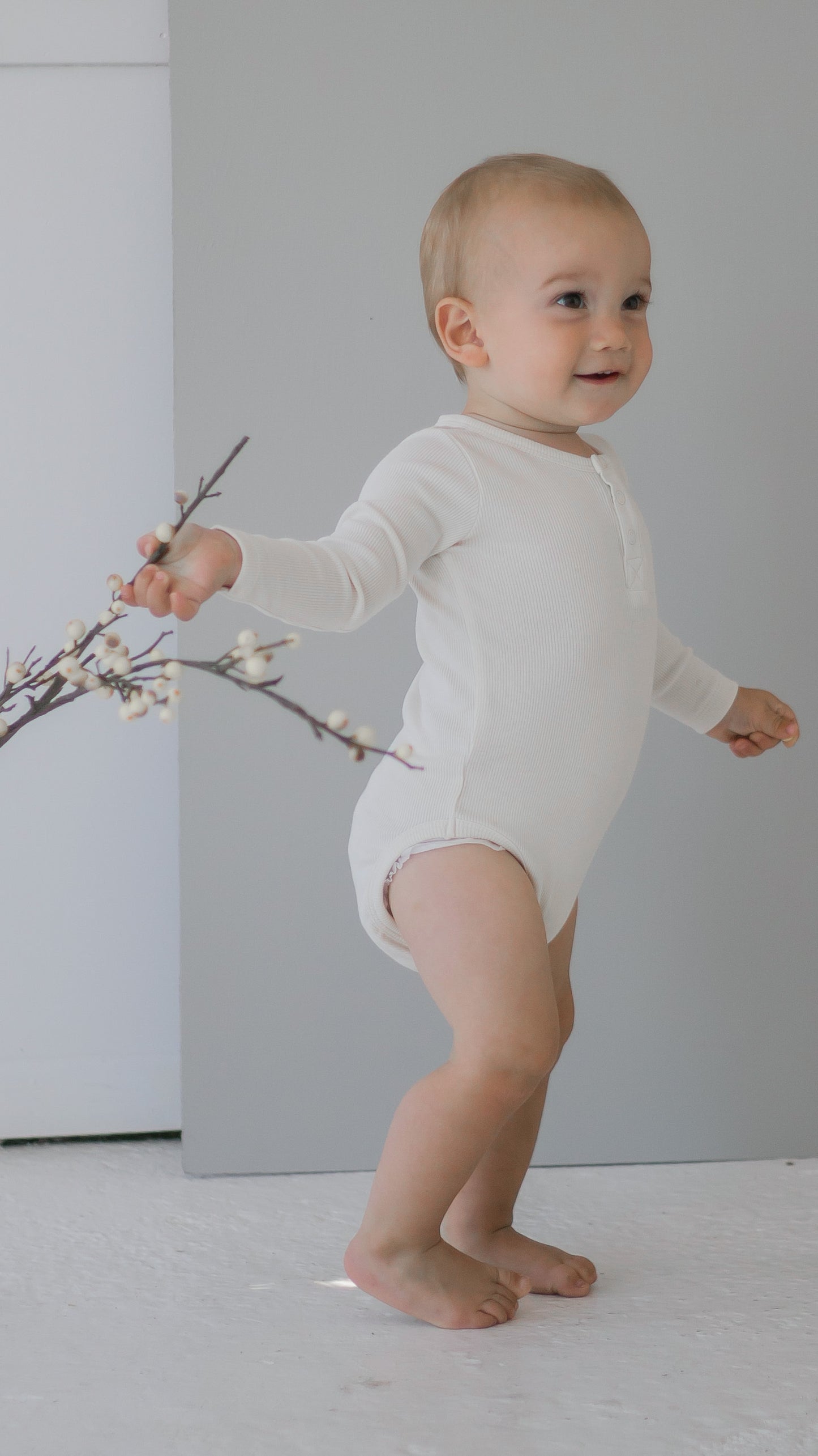 Girl standing against a grey background wearing a Long Sleeve Henley Rib Bodysuit in Dusty Rose, designed by Burrow and Be