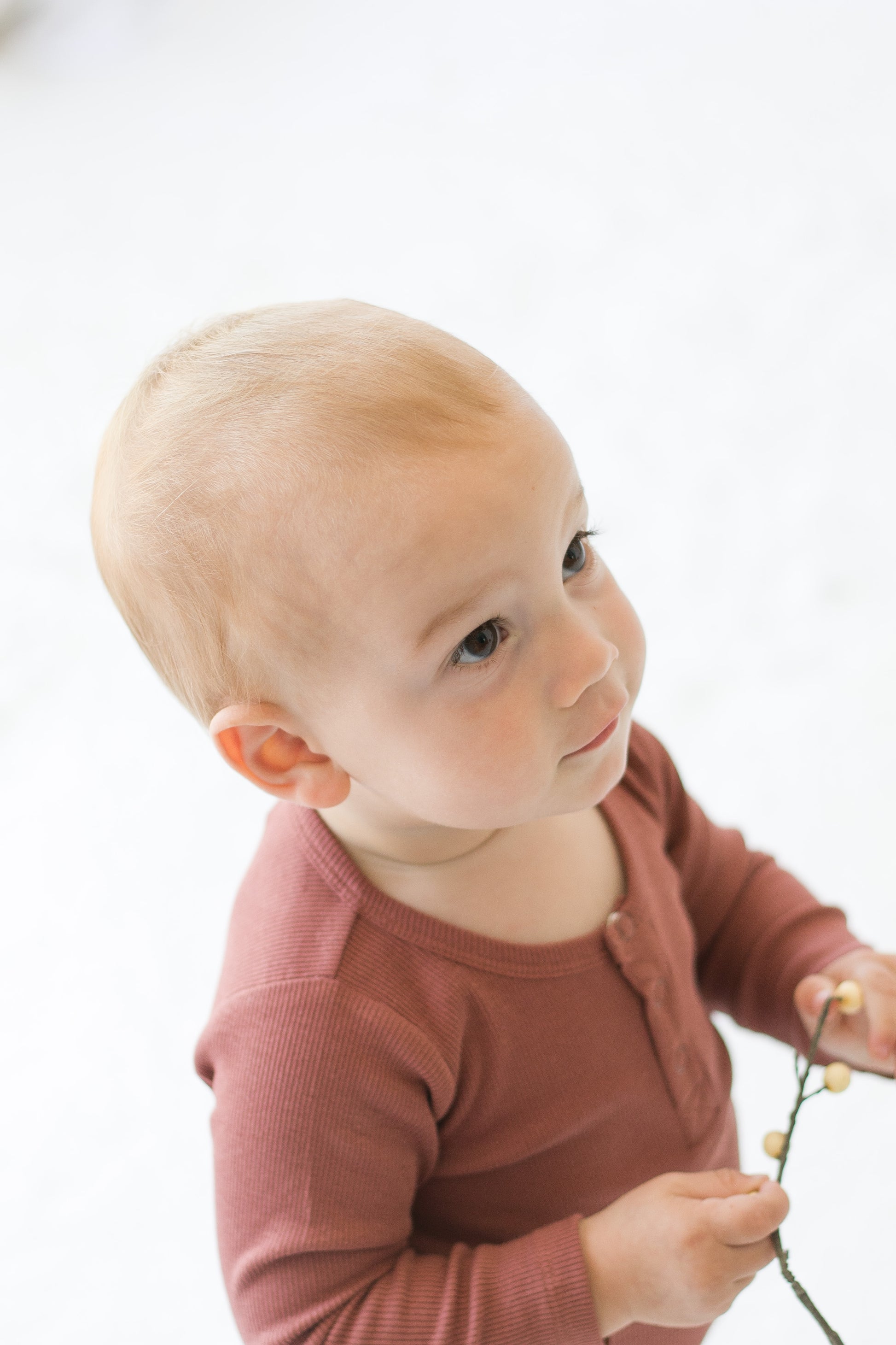 Boy standing on white carpet against a white background while wearing a Long Sleeve Henley Rib Bodysuit and Leggings in Clay, designed by Burrow and Be