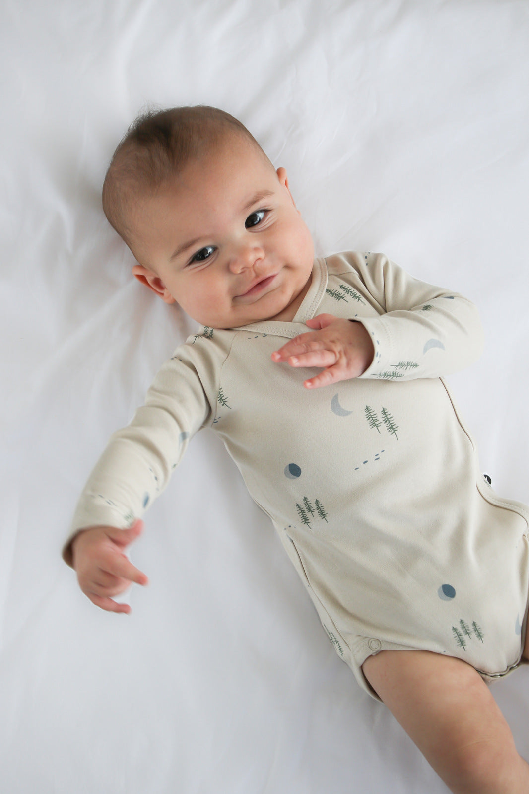 Baby laying on white sheets and posing in Midnight Forest Kimono Bodysuit, designed by Burrow and Be