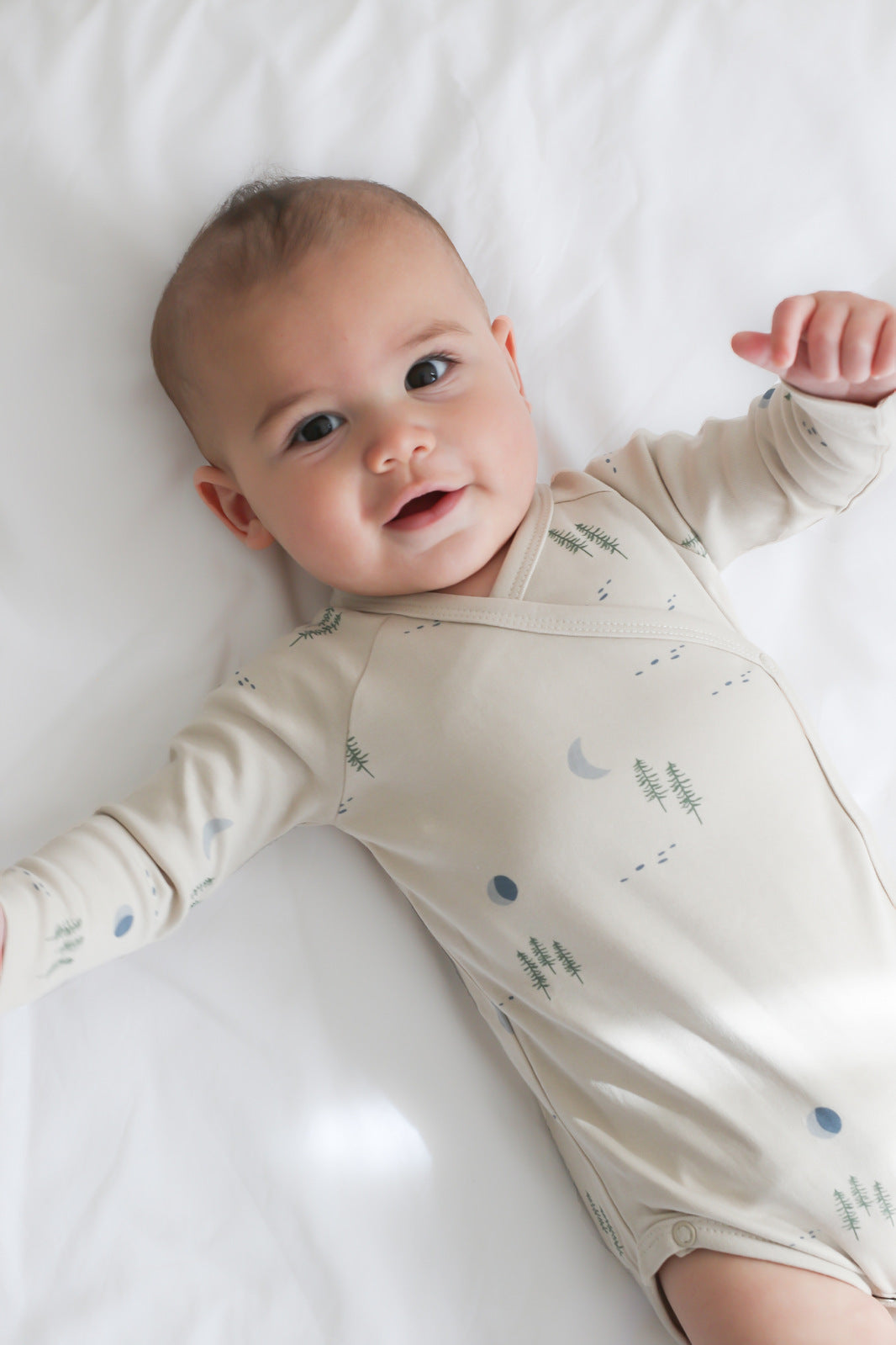 Baby laying on white sheets and wearing Midnight Forest Kimono Bodysuit, designed by Burrow and Be