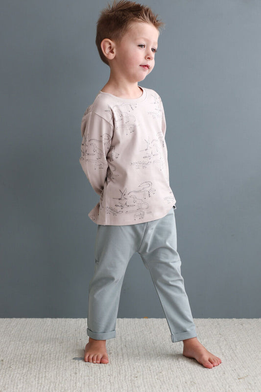 Child wearing a light pink long-sleeve shirt and light blue pants against a gray background