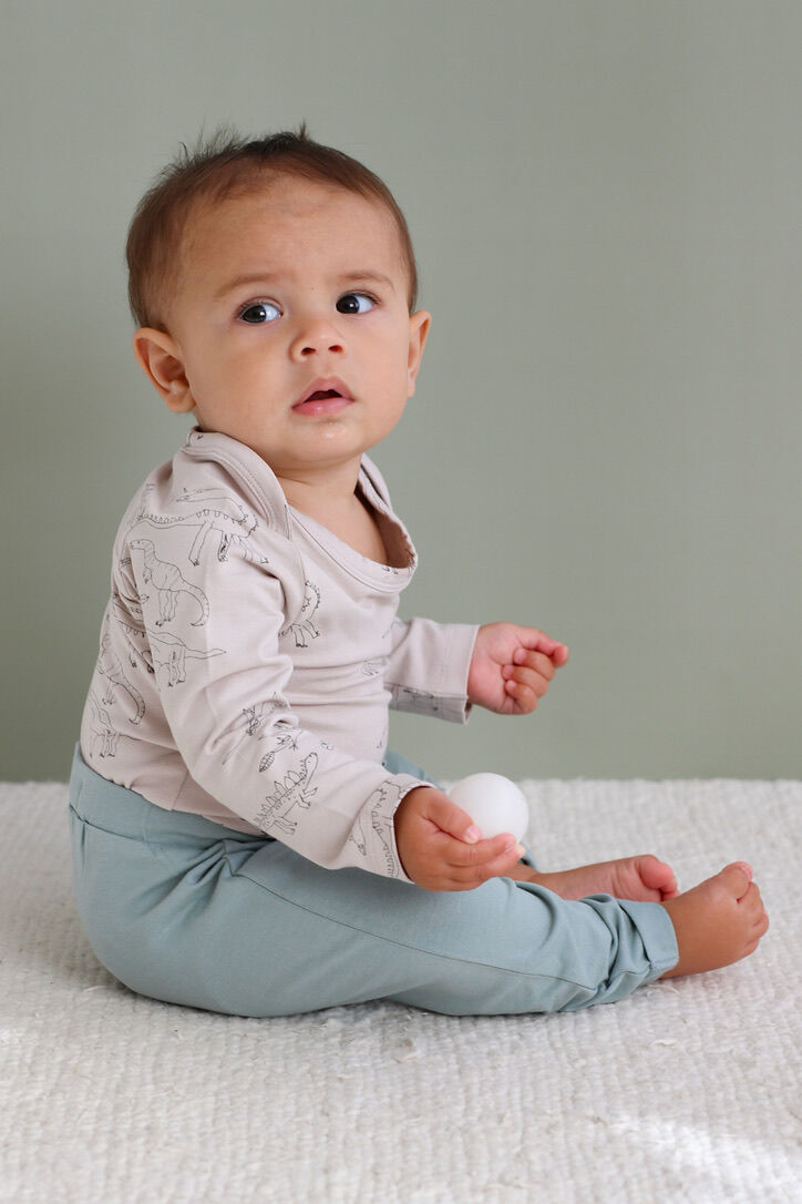 Baby sitting on a textured surface wearing a light pink top and light blue pants.