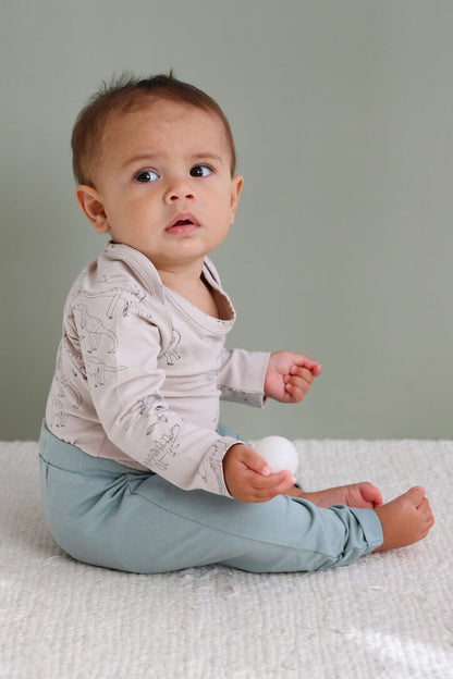 Baby sitting on a textured surface wearing a light pink top and light blue pants.