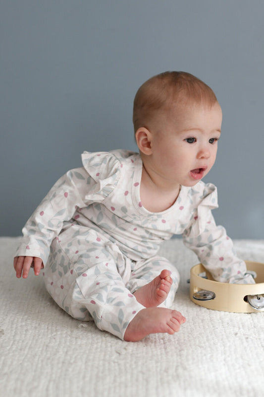 Baby in a white outfit with ruffles sitting on a textured surface with a gray background