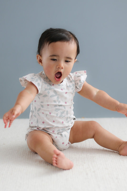 Baby sitting on a white surface wearing a patterned onesie against a gray background