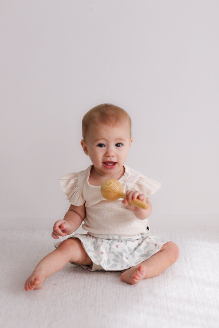 Baby sitting on a white surface holding a wooden toy