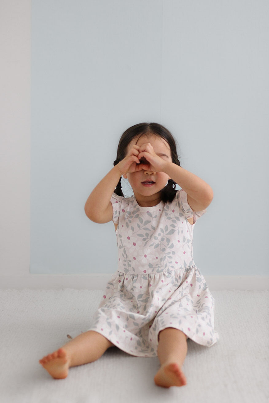 Child in a floral dress sitting on a light gray surface with a light blue wall background