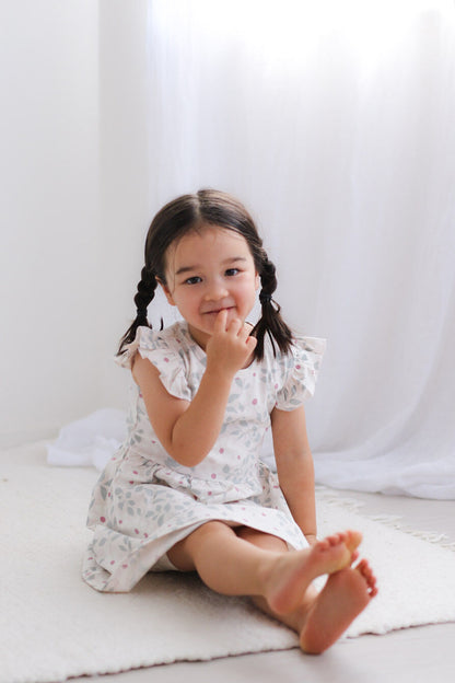 Young girl in a floral dress sitting on a white surface with a white curtain background