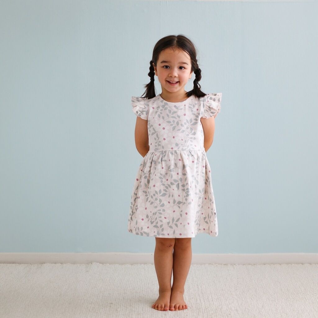Young girl wearing a floral dress against a light blue wall