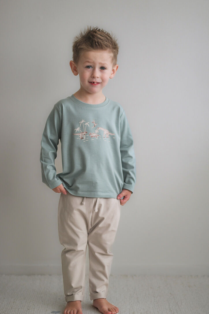 Young boy wearing a light green long-sleeve shirt and beige pants against a plain background
