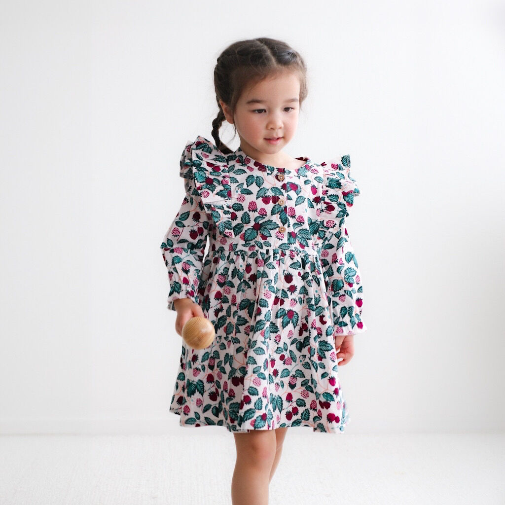 Young girl wearing a floral dress holding a wooden toy on a white background