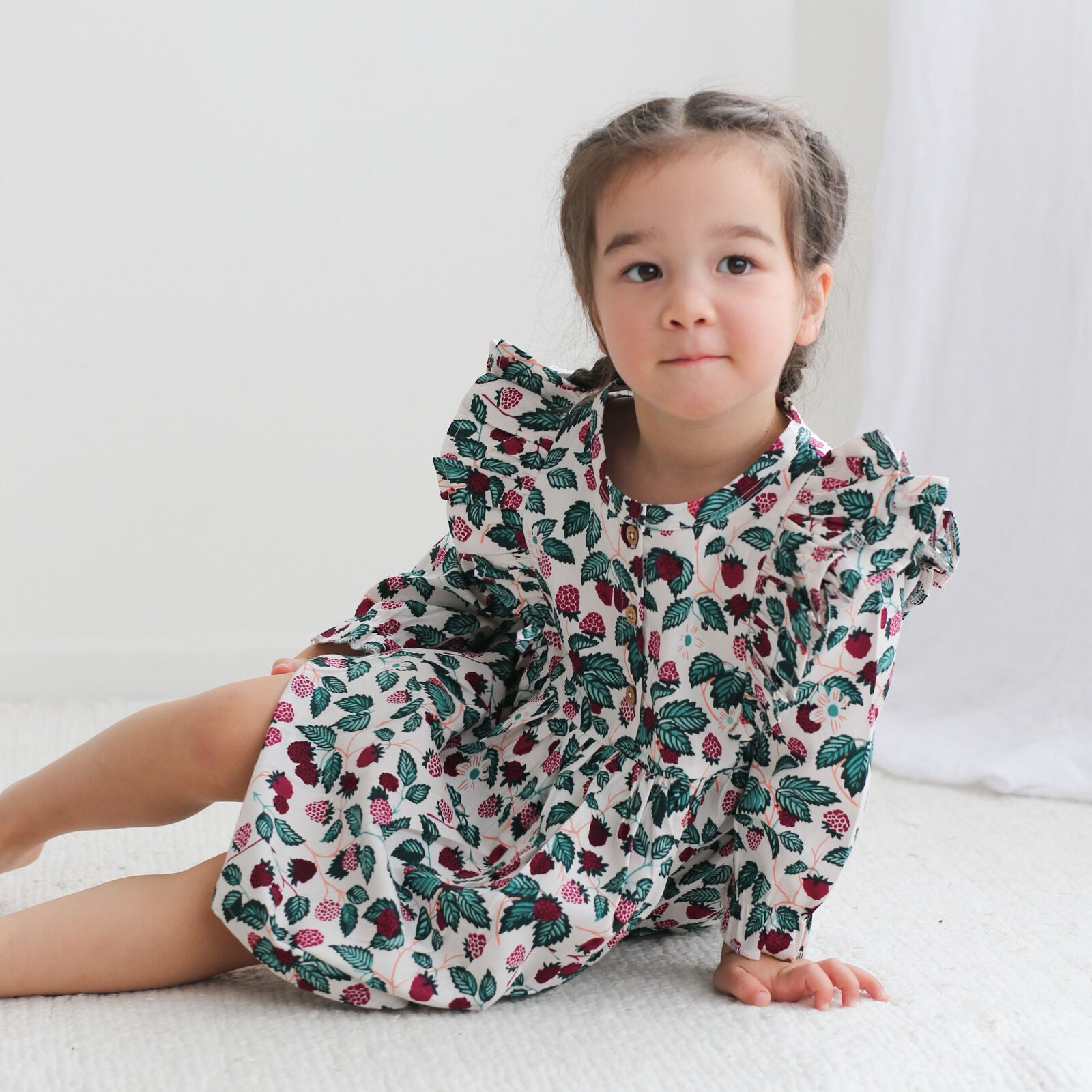 Young girl wearing a floral dress sitting on a white surface
