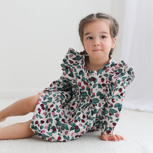 Young girl wearing a floral dress sitting on a white surface