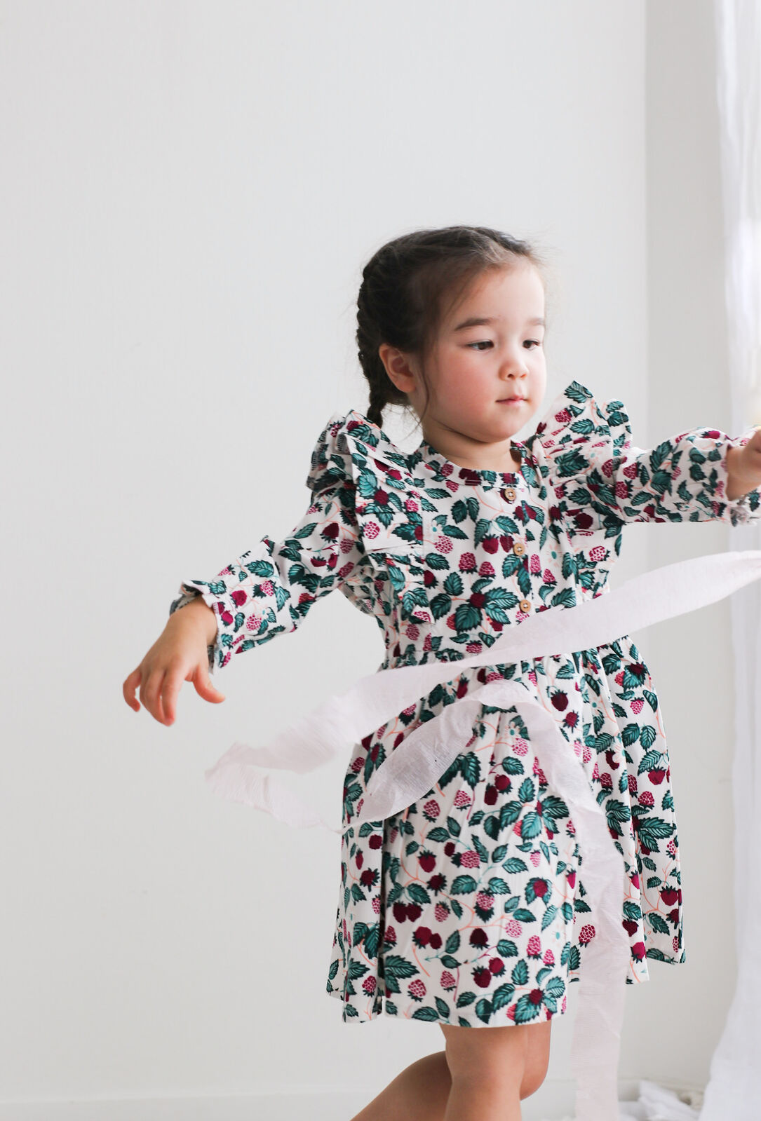 Young girl wearing a floral dress with long sleeves against a white background