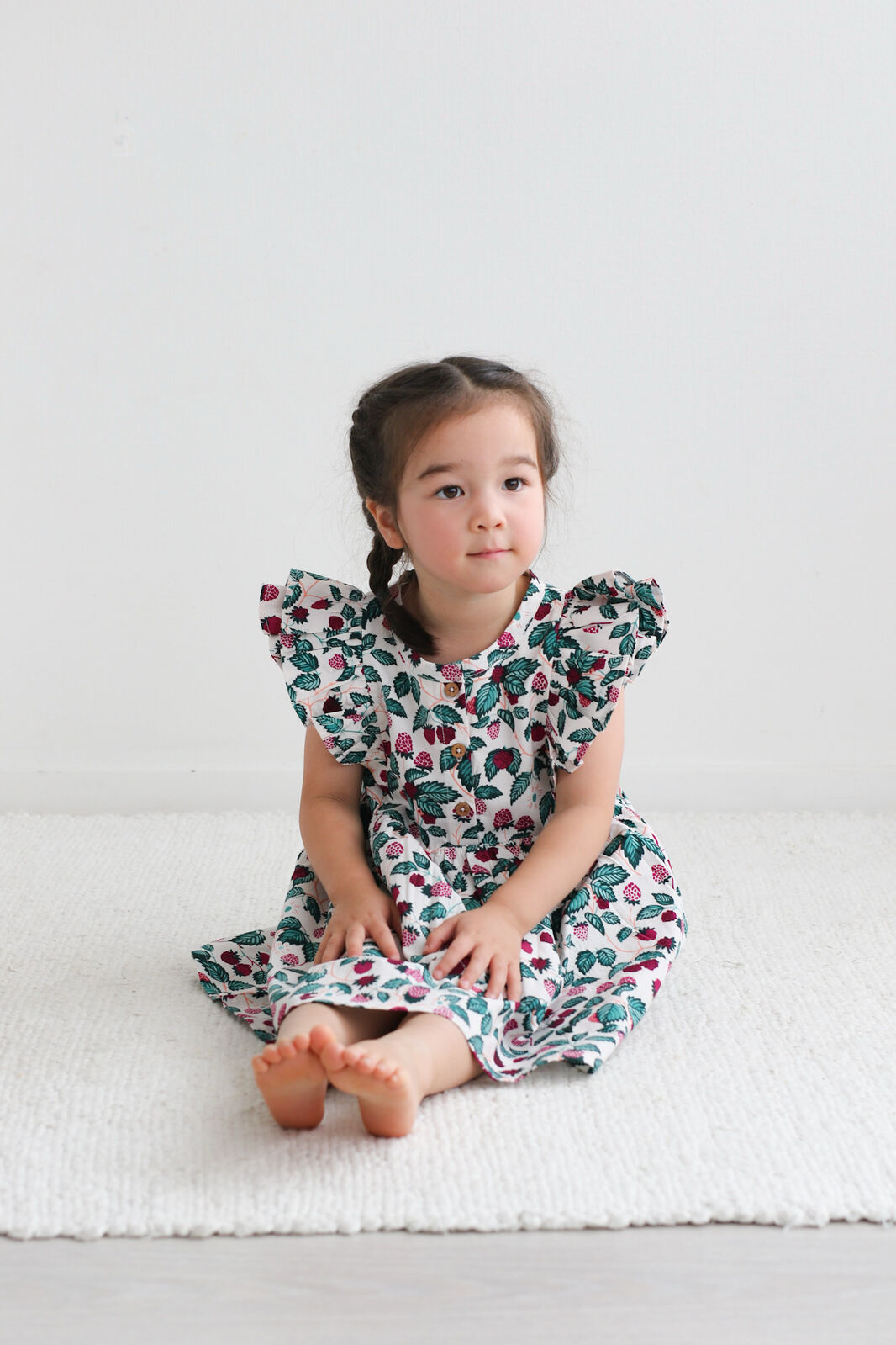 Young girl wearing a floral dress sitting on a white surface.