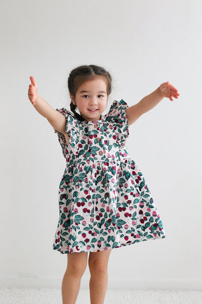 Child wearing a floral dress with arms raised on a plain background