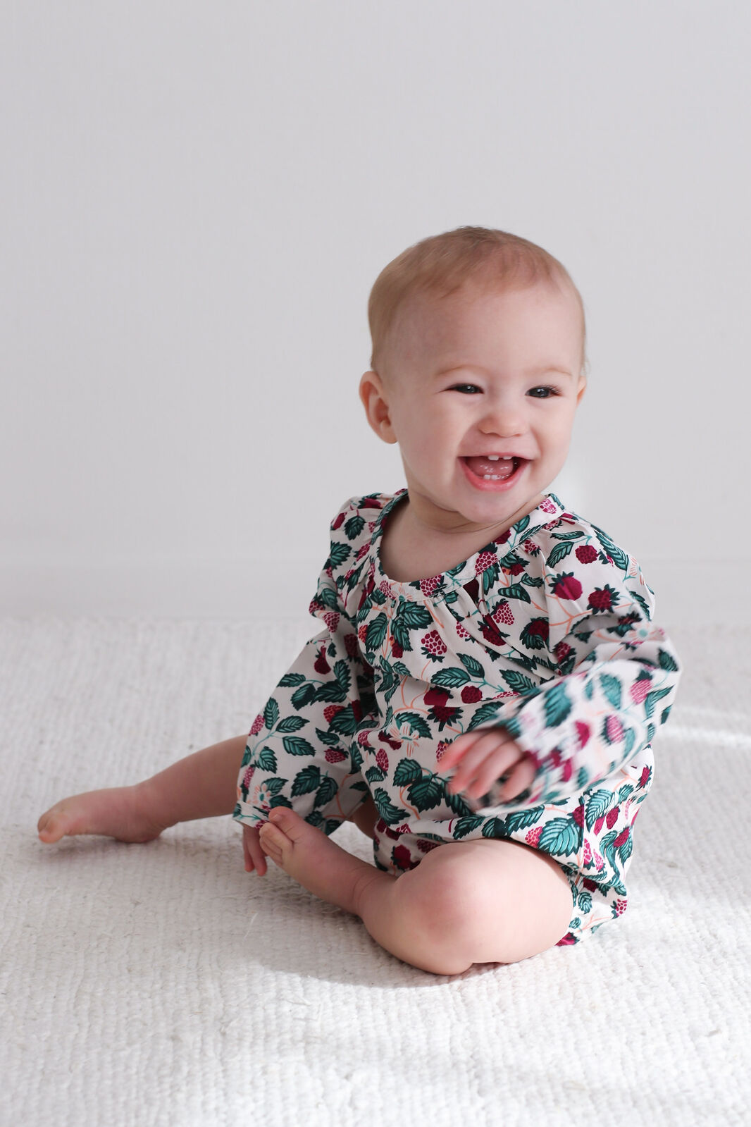 Baby wearing a floral onesie sitting on a white surface