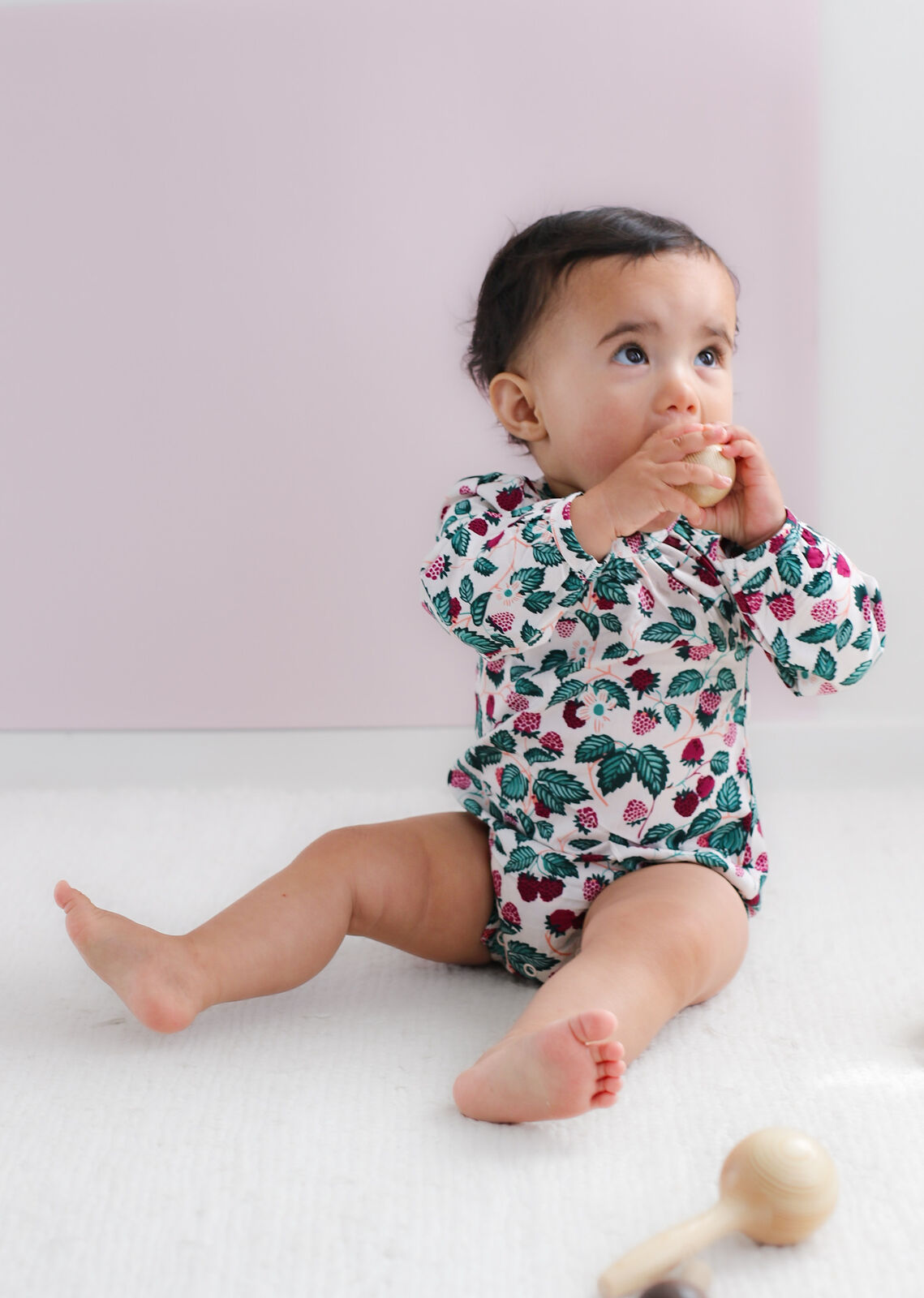 Baby wearing a floral onesie sitting on a white surface with a pink background