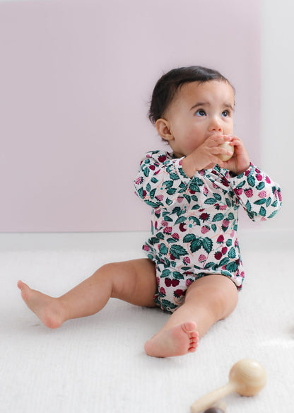 Baby wearing a floral onesie sitting on a white surface with a pink background
