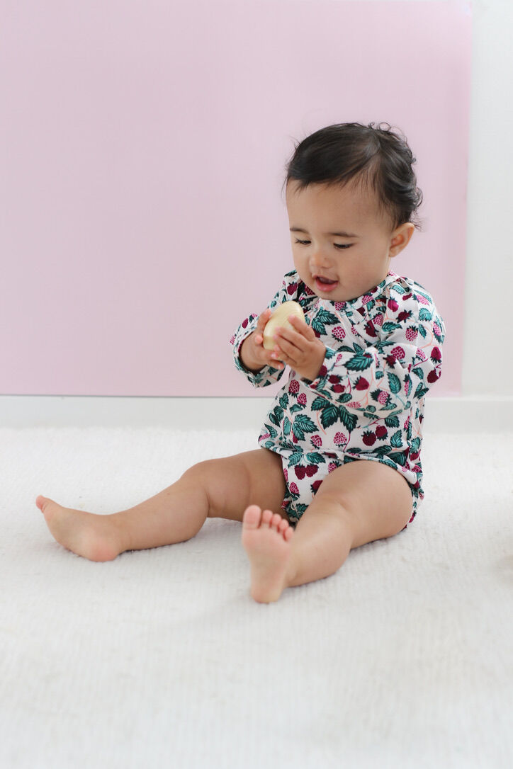 Baby in a floral onesie sitting on a white surface with a pink background