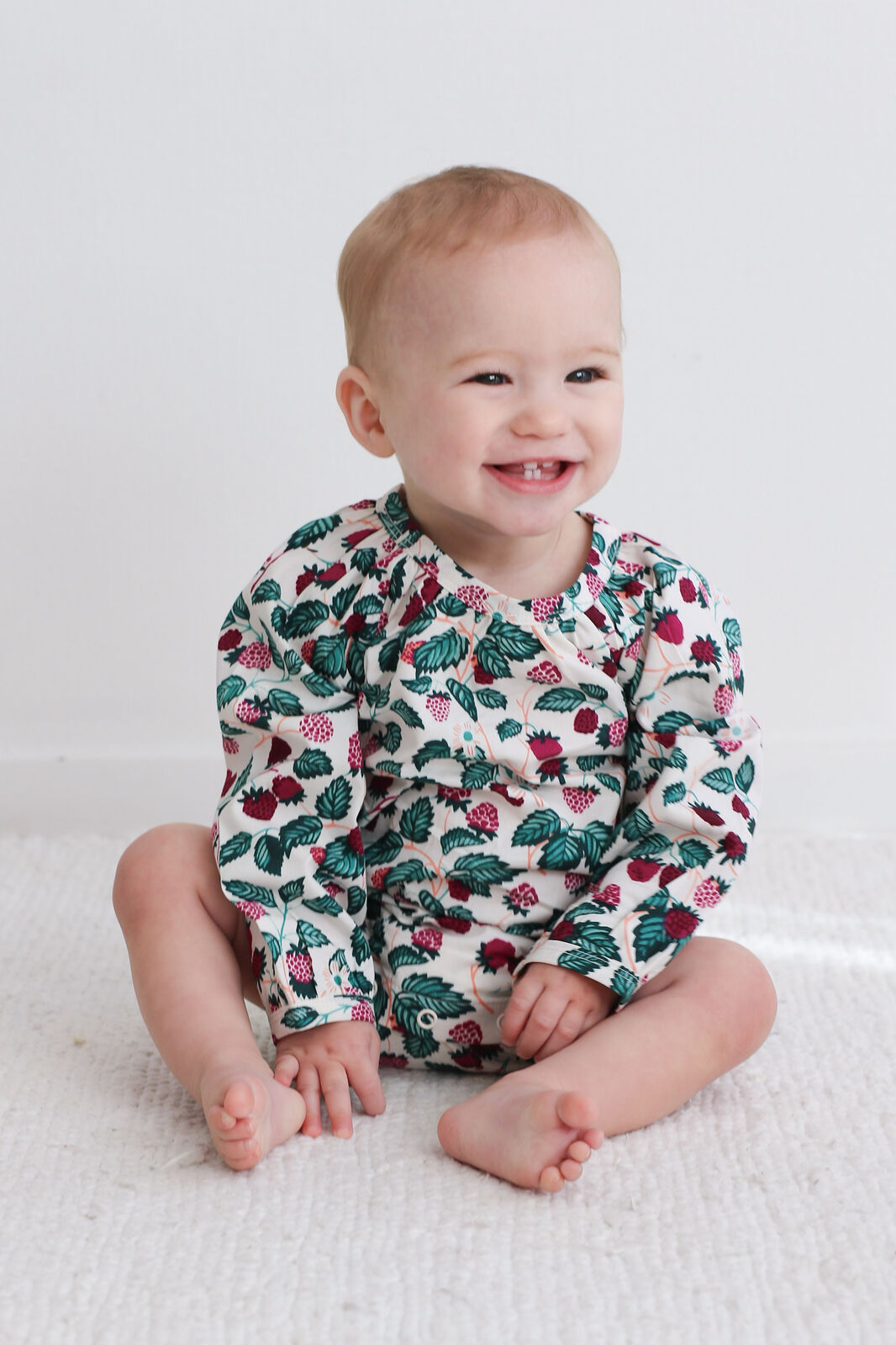 Baby wearing a cactus-patterned onesie sitting on a white blanket.