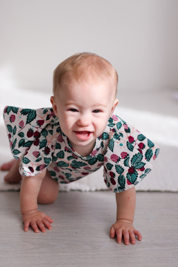 Baby crawling on a light-colored floor wearing a floral outfit.