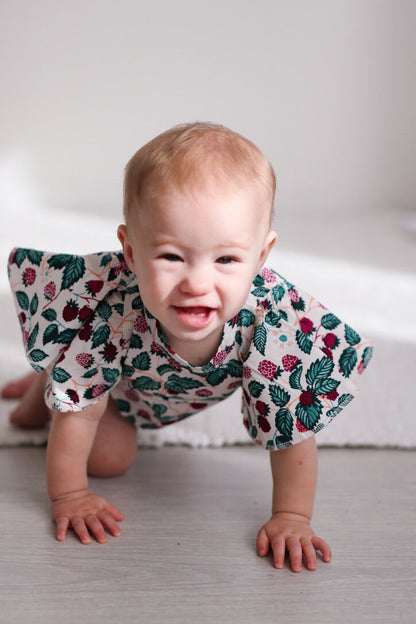Baby crawling on a light-colored floor wearing a floral outfit.