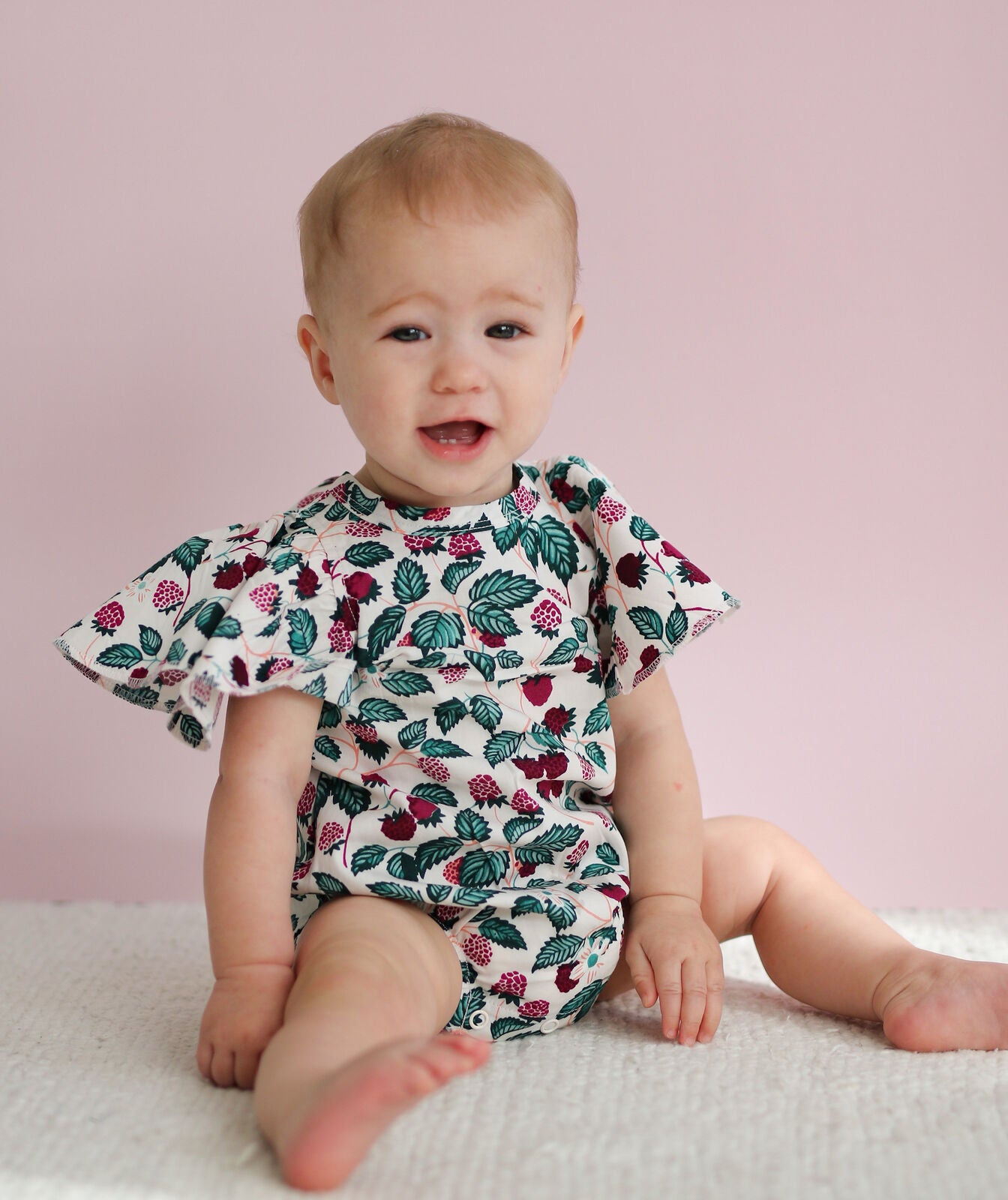 Baby wearing a floral romper sitting on a light pink background