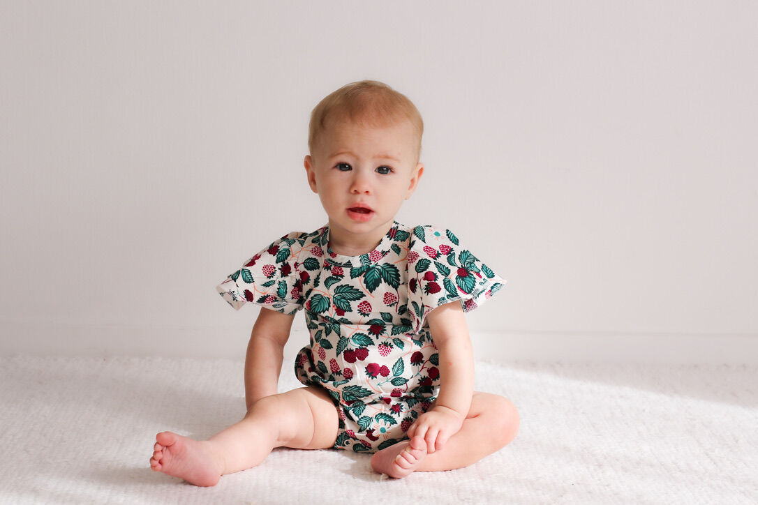 Baby wearing a floral onesie sitting on a white blanket