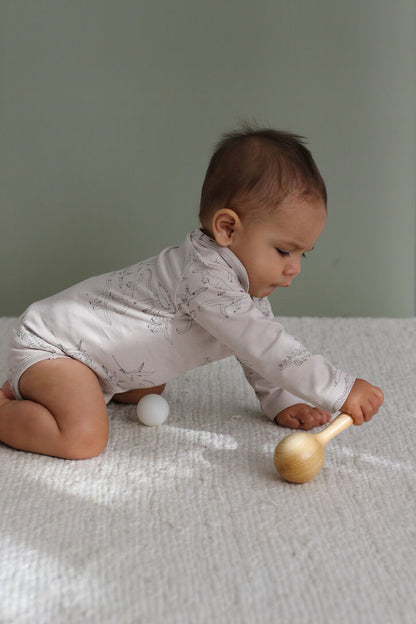 Baby playing with a wooden toy on a white blanket