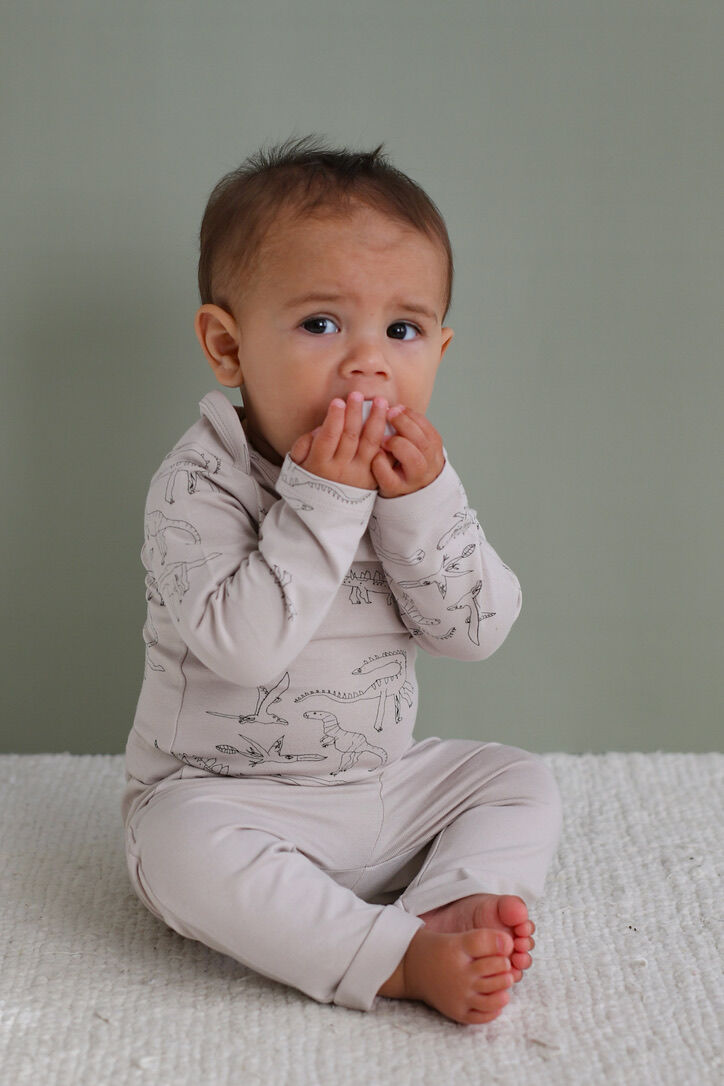 Baby wearing a light gray outfit with patterns, sitting on a textured surface against a plain background.