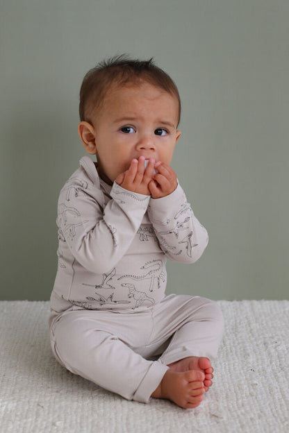 Baby wearing a light gray outfit with patterns, sitting on a textured surface against a plain background.