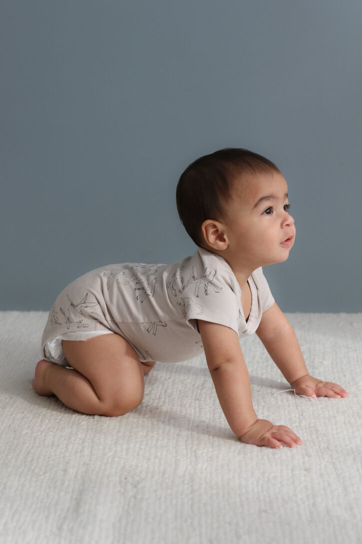 Baby in a light-colored onesie crawling on a textured surface with a gray background