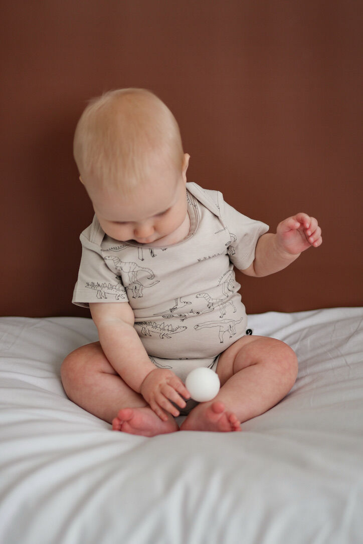 Baby sitting on a bed holding a white ball against a brown background