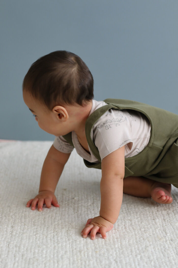 Baby in a green vest crawling on a textured surface with a gray background