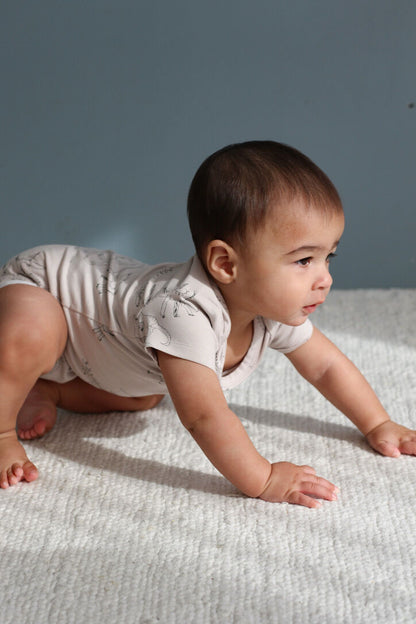 Baby in a light-colored outfit crawling on a textured surface with a neutral background