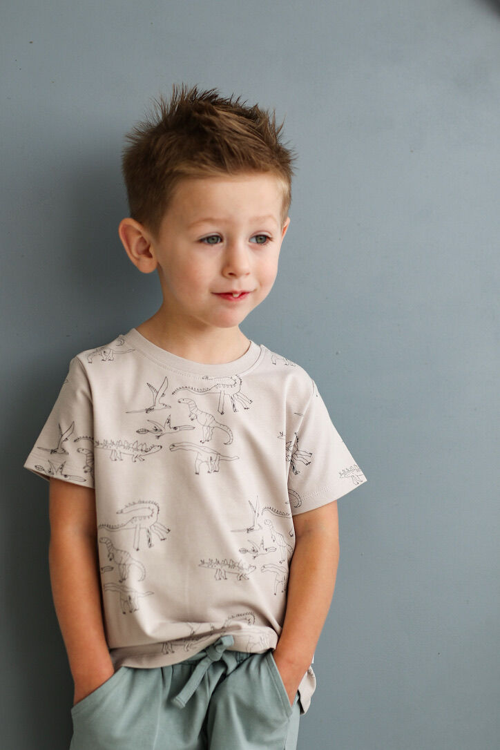 Young boy wearing a light-colored t-shirt with graphics against a gray background