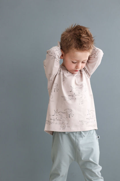 Child wearing a light pink shirt with animal prints and light blue pants against a gray background