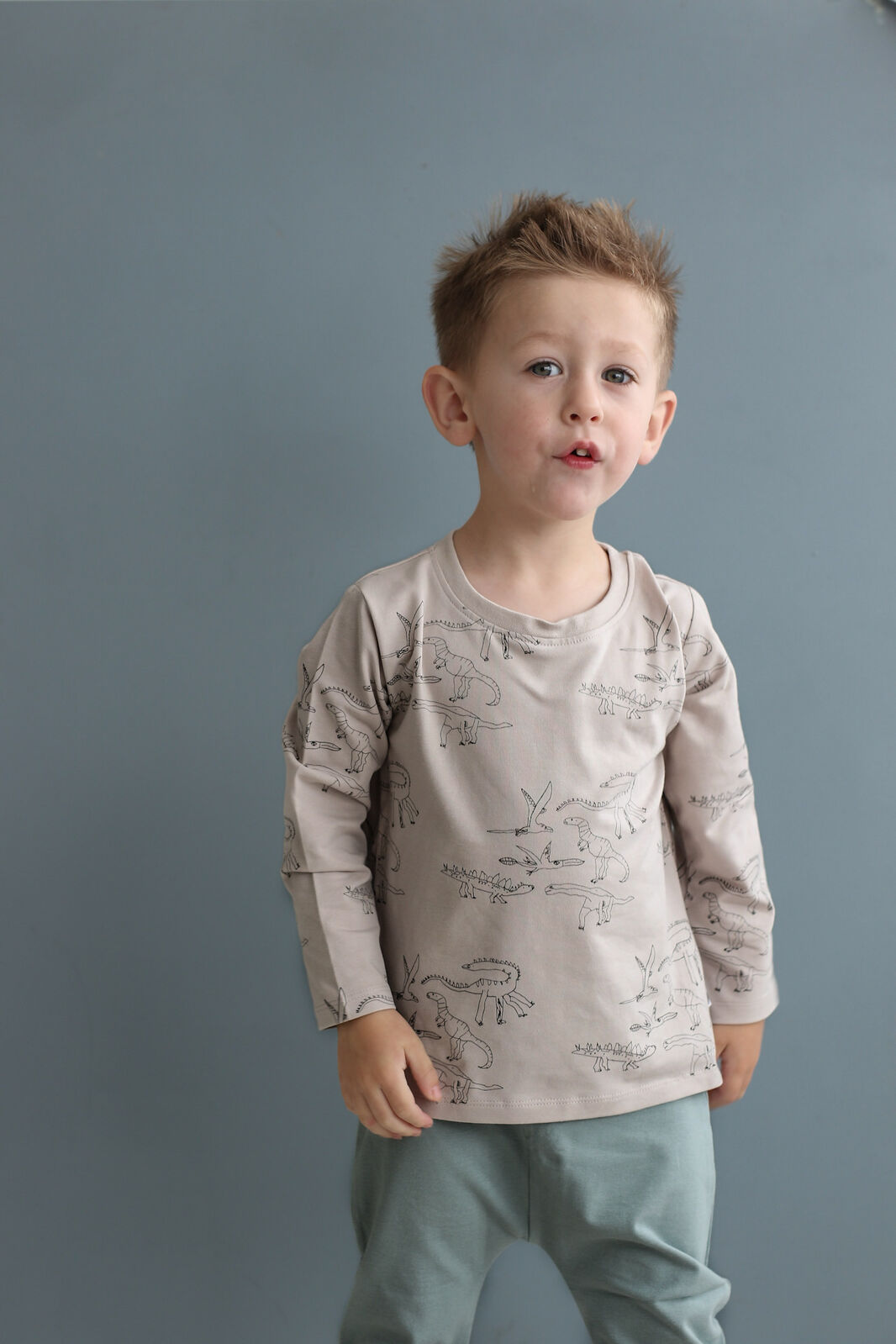 Young boy wearing a patterned shirt and light pants against a gray background