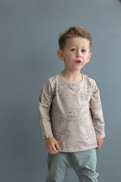 Young boy wearing a patterned shirt and light pants against a gray background