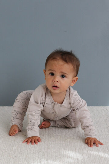 Baby in a light gray outfit crawling on a white surface with a blue wall background