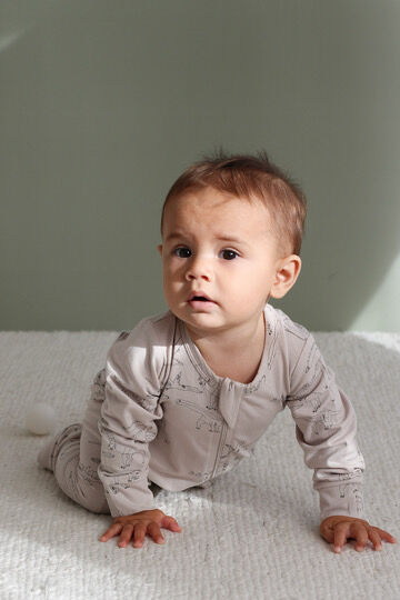 Baby in a light gray onesie crawling on a white blanket with a neutral background