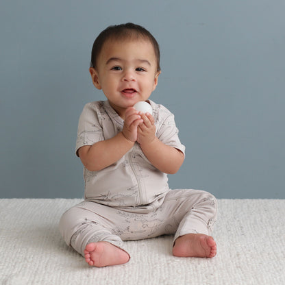 Baby sitting on a white blanket holding a white ball against a gray background