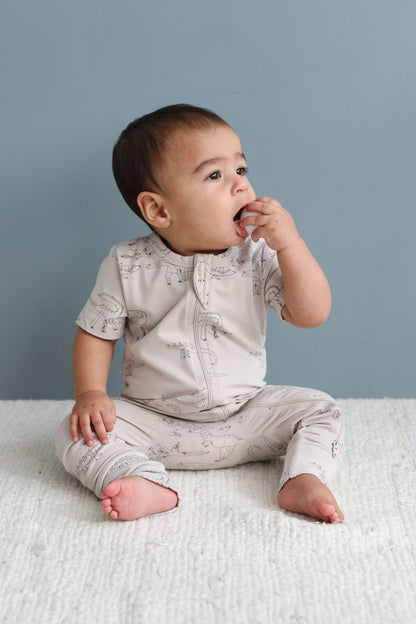 Baby in a light gray outfit sitting on a white surface with a blue background